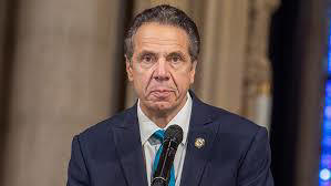 Andrew Cuomo sitting in front of a microphone looking like he has done something wrong;