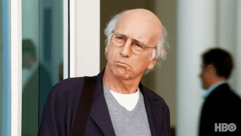 Curb Your Enthusiasm Larry David standing outside an office shrugging his shoulders;