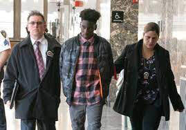 Luchiano Lewis walking in handcuffs next to two officers;