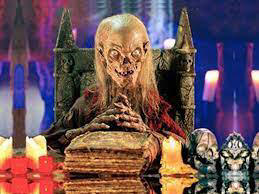 Tales From The Crypt Crypt Keeper sitting down with a big book on the table;